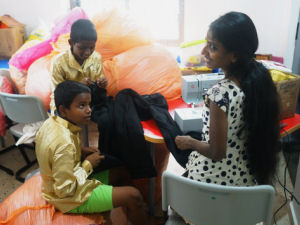 Couple of kids sat amonst SOME of the donated clothes getting their trousers altered