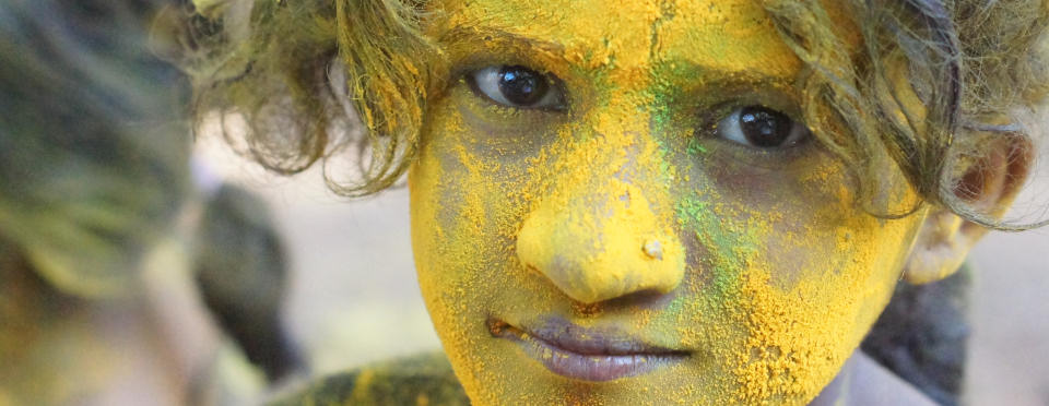 A young girl with bright yellow Holi powder covering her face