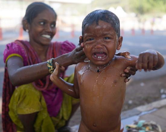 A Slum child being washed on the footpath next to a busy road